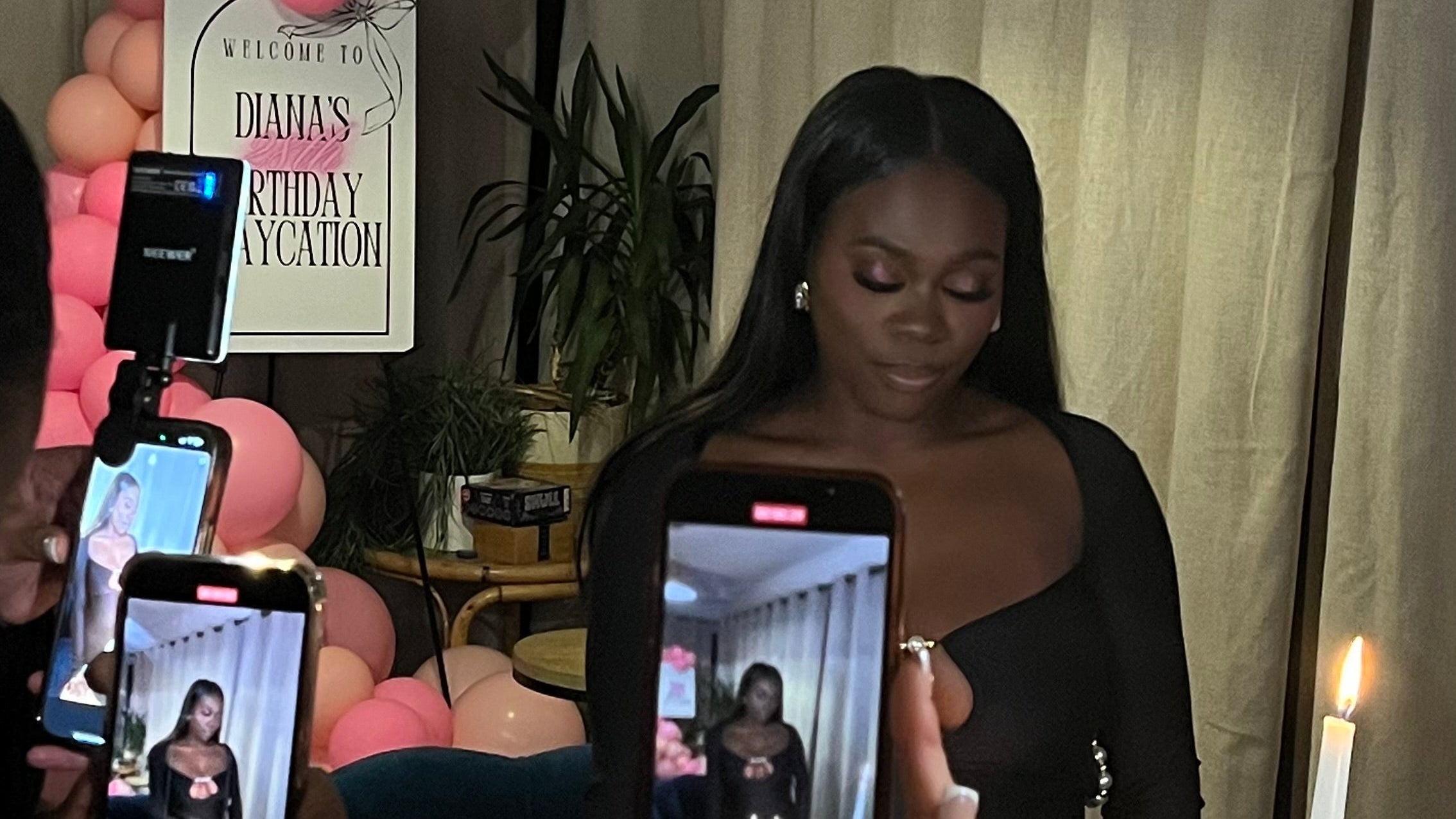 Woman being photographed by multiple people with smartphones in a room with balloons and decor.